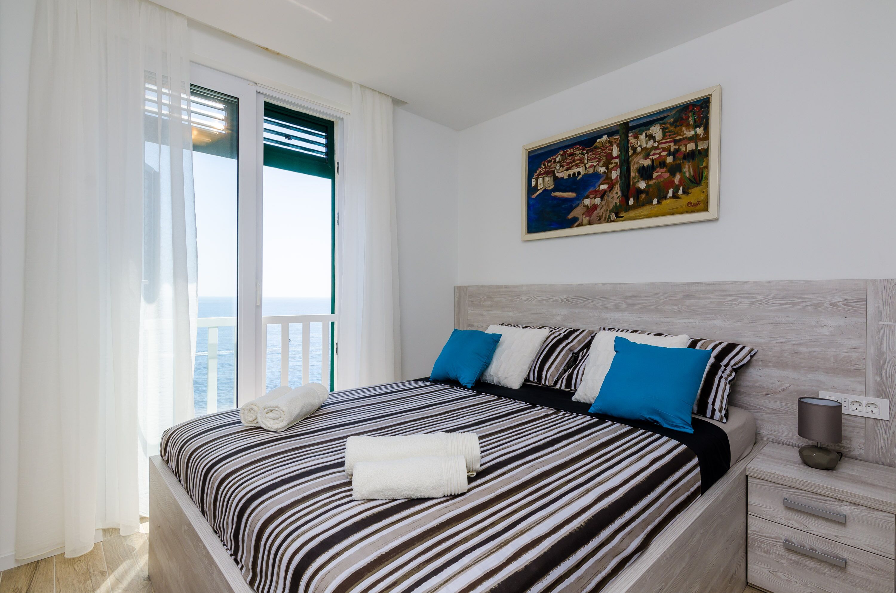 Quarto de hotel moderno com uma cama grande, um quadro na parede e uma varanda com vista.