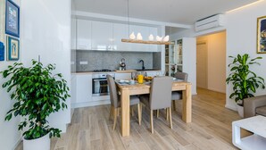 A modern kitchen with white cabinets, a wooden dining table, and a hanging light fixture. - Apartments Lazarin (Dubrovnik)
