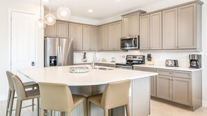 A modern kitchen with a large island, stainless steel appliances, and light-colored cabinetry.