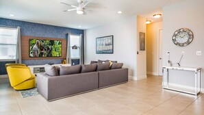 A modern living room with a grey sectional sofa, a yellow armchair, and a flat-screen TV mounted on the wall.
