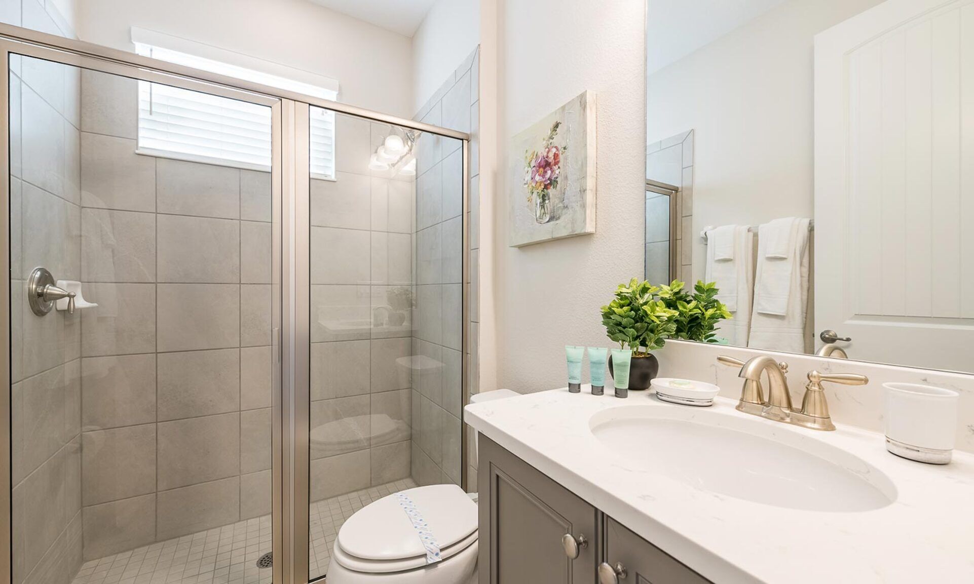 A modern bathroom with a glass-enclosed shower, a white sink with gold faucets, and a large mirror.