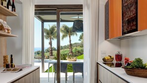 A modern kitchen with a view of a patio, a dining area, and a kitchen counter with various items. - Rocco Forte Private Villas (Sciacca)