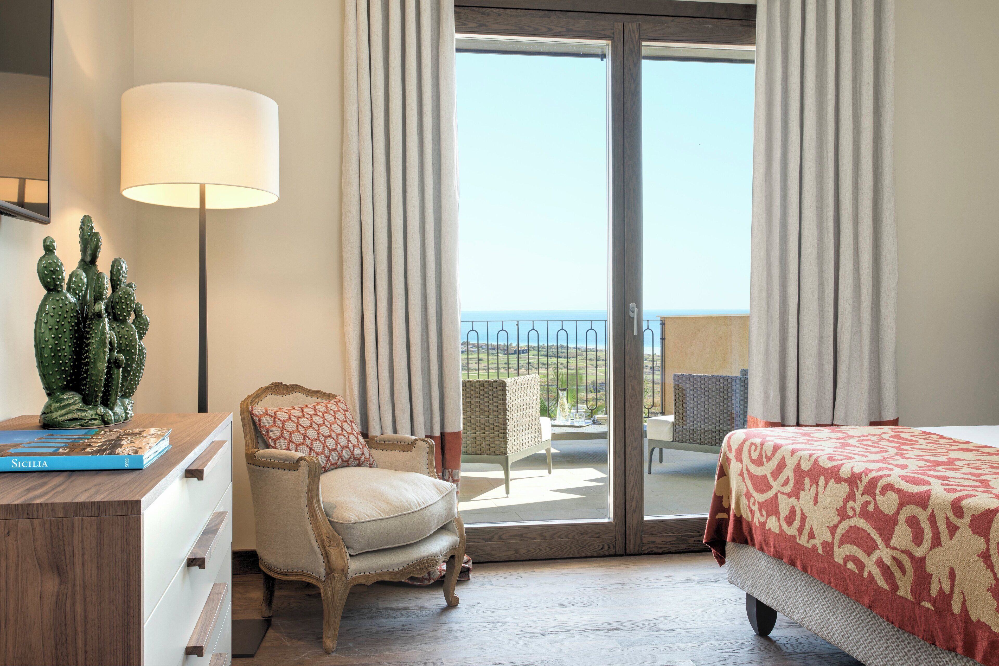 Une chambre d’hôtel avec un lit, une chaise, un bureau, une sculpture de cactus et une vue sur la mer.