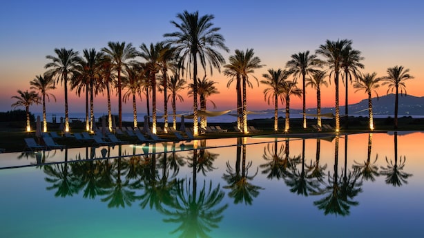 A poolside area with lounge chairs and palm trees at sunset. - Rocco Forte Private Villas (Sciacca)