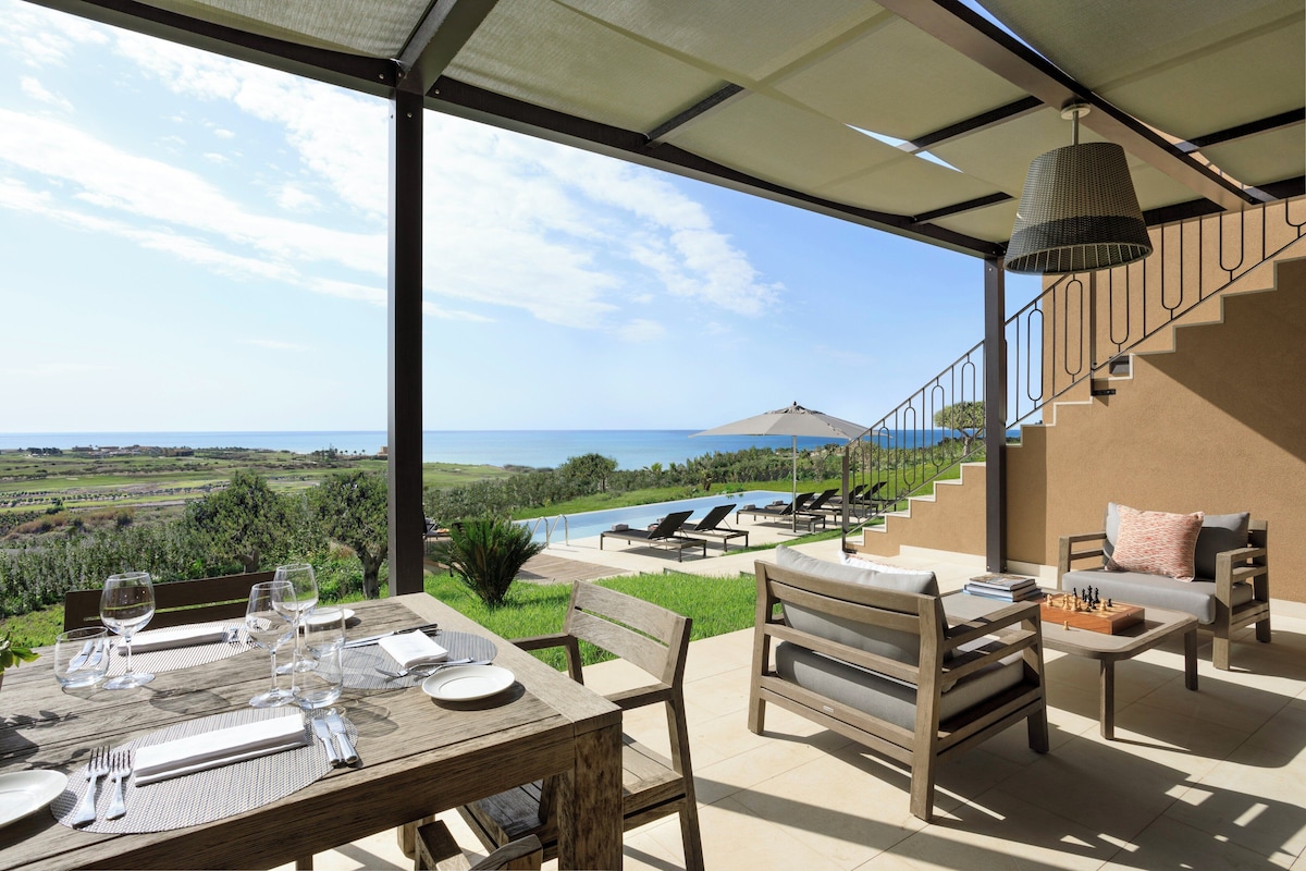 A dining area with a table set for four, overlooking a pool and a scenic landscape.