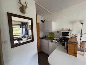 A compact kitchen with a window, a microwave, a sink, and a small cabinet.