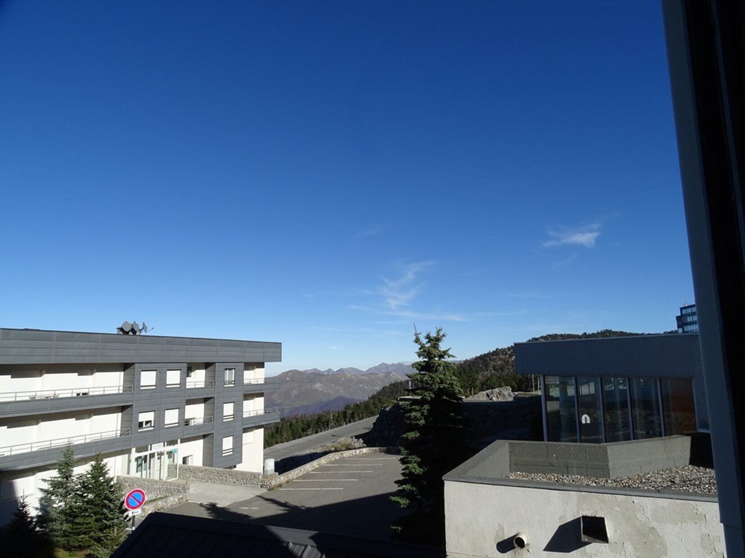 Un bâtiment moderne doté d’un toit plat, d’un espace de stationnement et ayant une chaîne de montagnes en toile de fond.