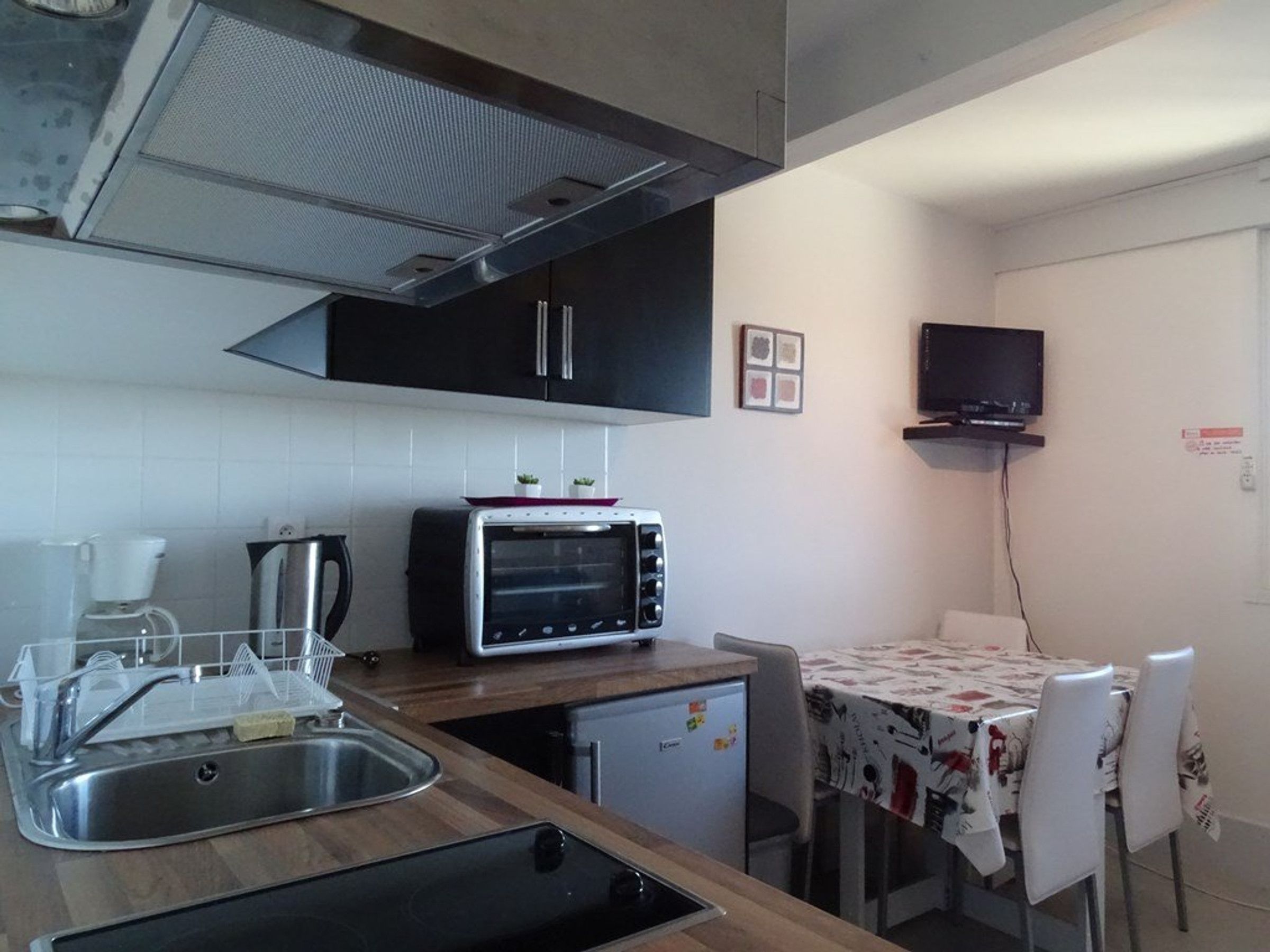 Eine kompakte Küche mit Einbauofen, Kaffeemaschine und kleinem Kühlschrank.