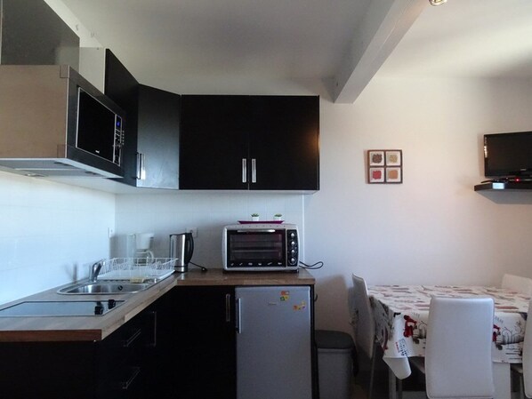 A compact kitchen with a microwave, toaster oven, and refrigerator. There is a small sink and a table with chairs.