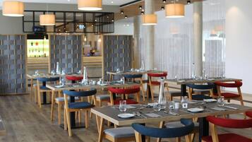 A modern restaurant with wooden tables and chairs, some with red cushions.