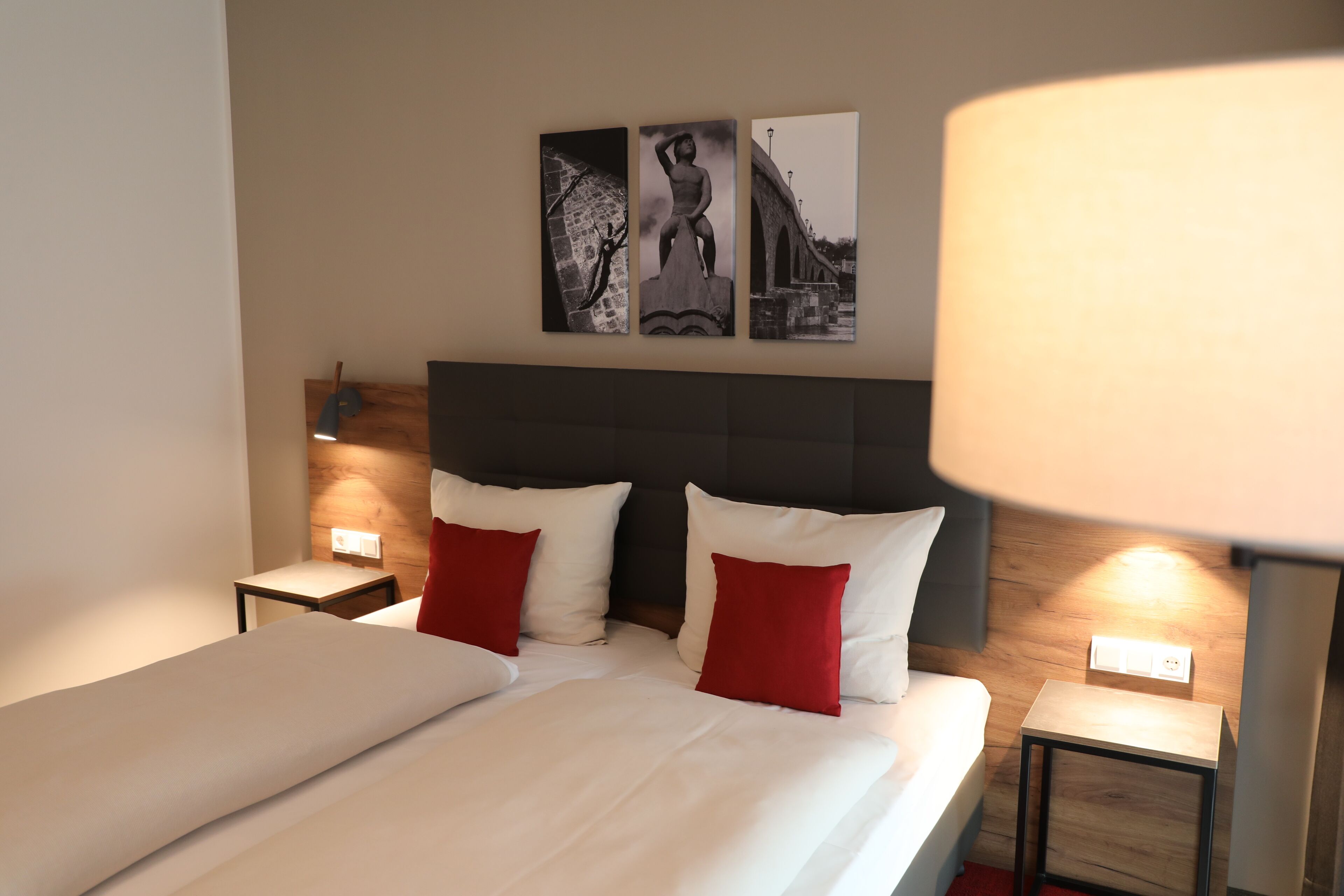 A hotel room with a large bed, two bedside tables, a nightstand, and three wall-mounted artworks.