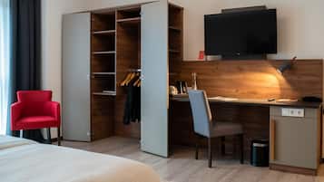 Habitación de hotel con cama, una silla roja, escritorio con silla, televisión y armario.