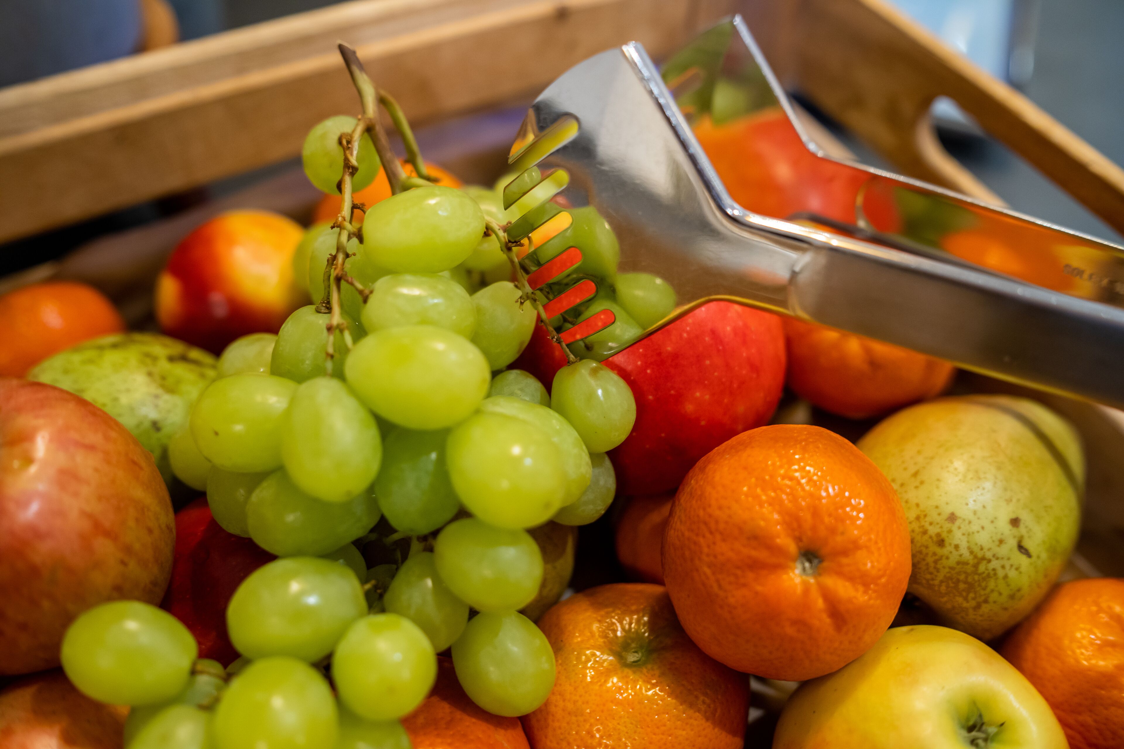 Una caja de madera llena de frutas variadas, como manzanas, naranjas y uvas.