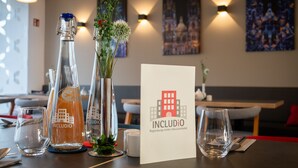 A hotel table set with clear glasses, a bottle, a menu, and a decorative vase. - Hotel INCLUDiO (Regensburg)