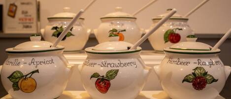 Une collection de pots en céramique blanche, ornés d’un bord vert et de motifs représentant des fruits, chaque pot étant étiqueté avec le nom d’un fruit différent.