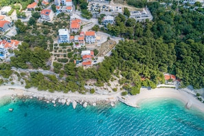 An aerial view of a coastal residential area with houses, a beach, and clear turquoise waters. - Rooms Sani (Brela)