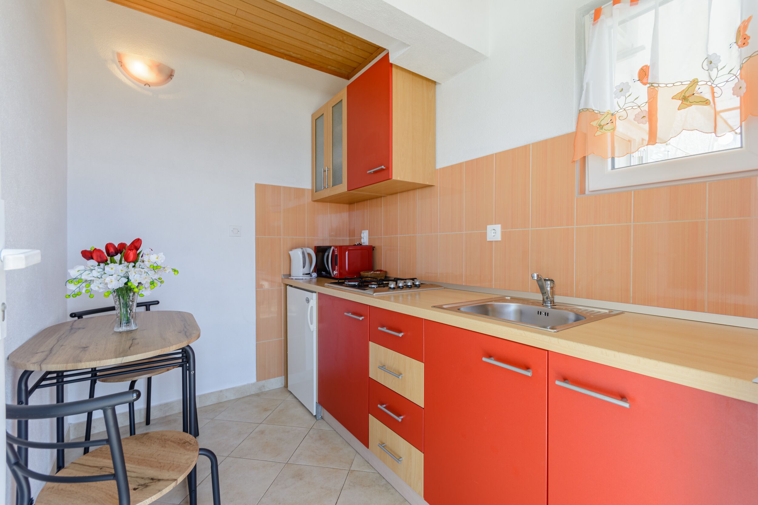A kitchen with red cabinets, a wooden countertop, a sink, and a dining table with chairs.