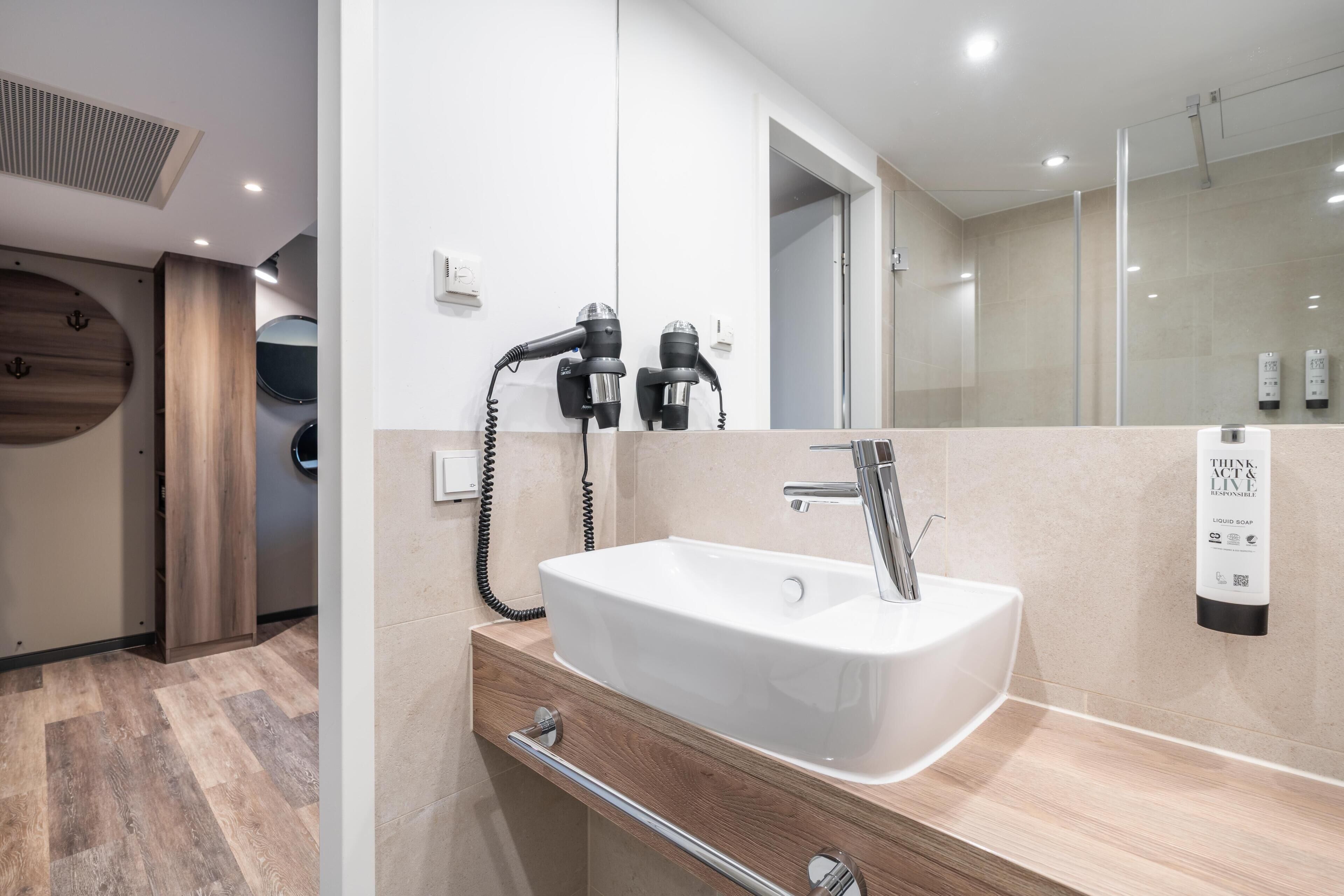 Een moderne badkamer met een witte wasbak, een spiegel en een haardroger.