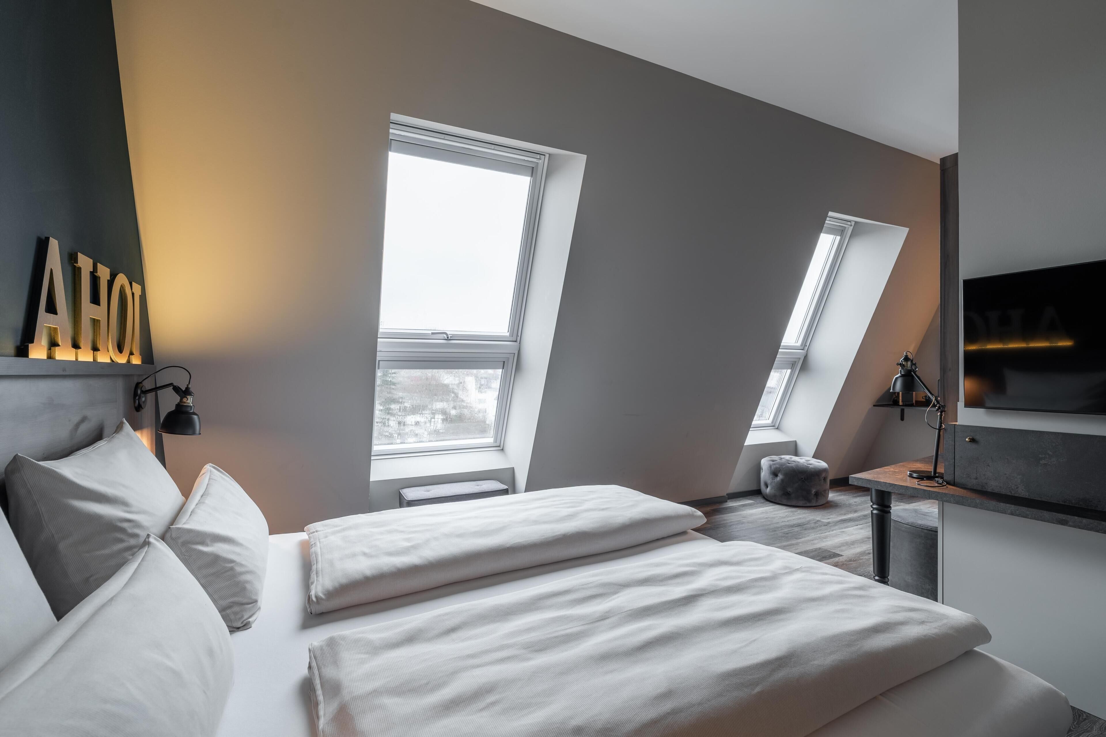 Ein modernes Schlafzimmer mit einem Bett, zwei Fenstern, einem Fernseher und einem Schreibtisch.