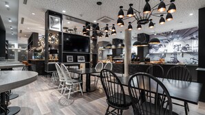 Un intérieur de restaurant moderne avec un espace de restauration central, des chaises noires et blanches, et des luminaires suspendus.