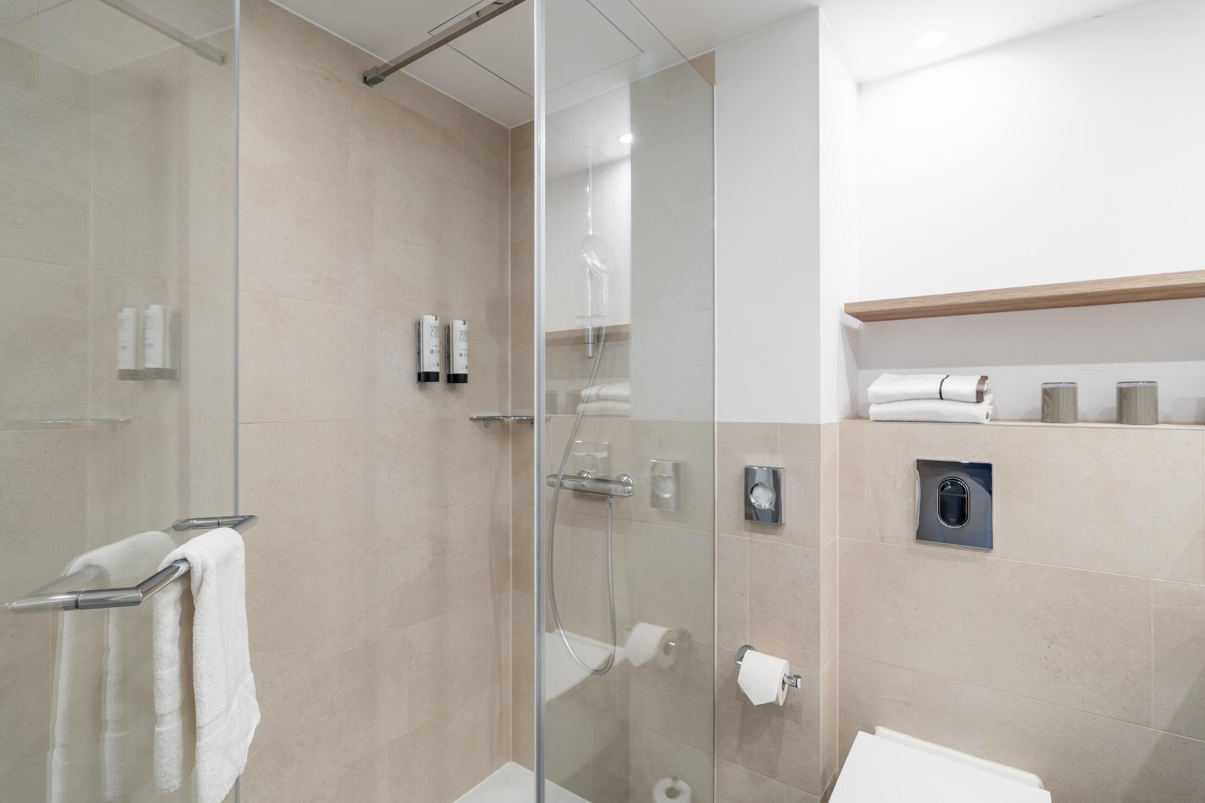 A modern bathroom with a glass shower enclosure, a toilet, and a shelf with toiletries.