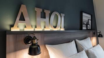 A bed with white pillows, a wall-mounted light fixture, and a wooden headboard.