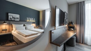 Une chambre d’hôtel moderne avec un lit aux lignes courbes, une table de chevet, un bureau et un grand miroir.