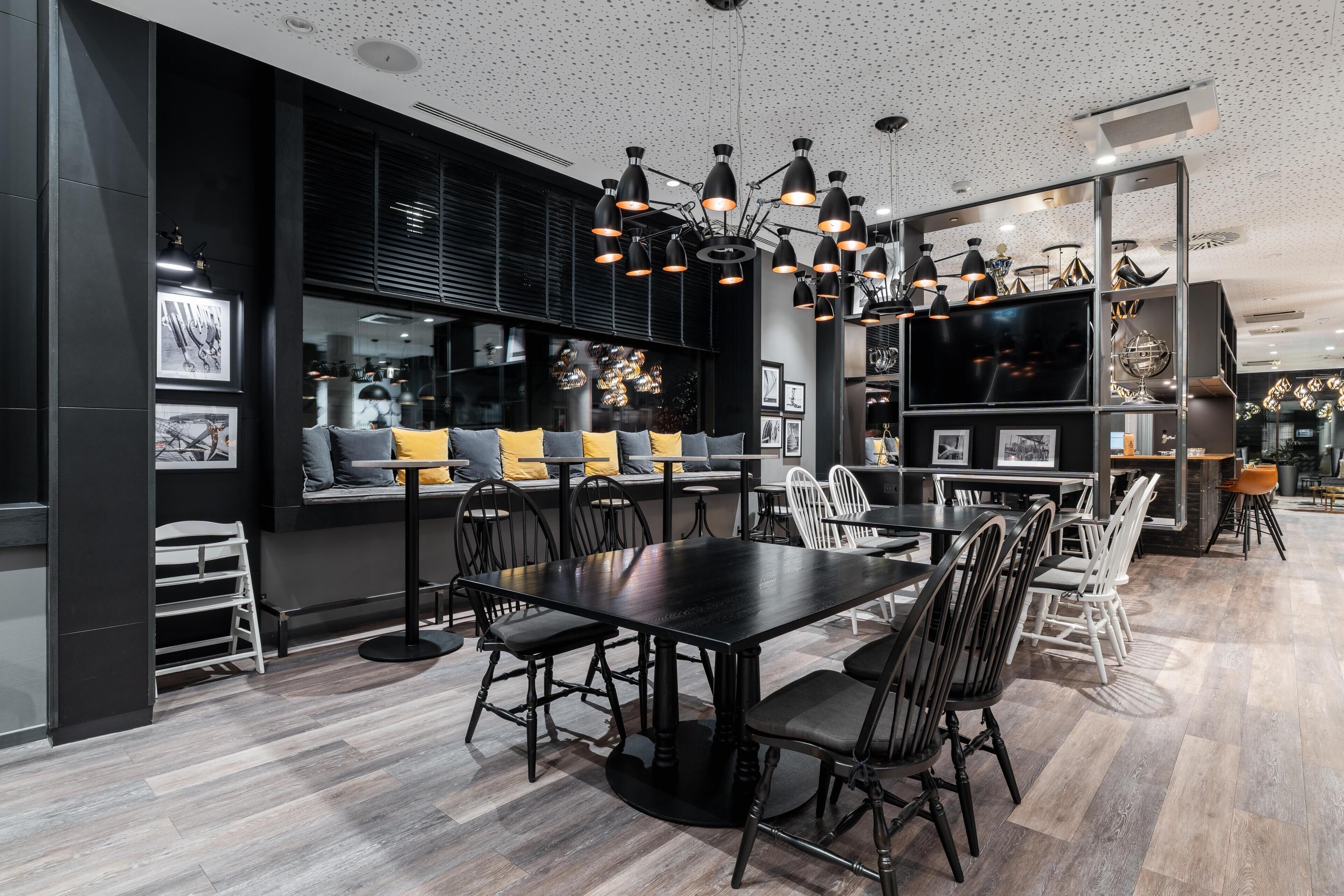 A modern dining area with a black table and chairs, a seating area with cushions, and a decorative ceiling light fixture.