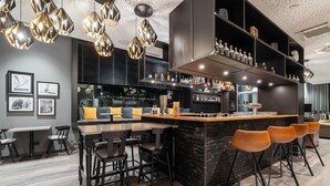 Un espace bar moderne doté d’un îlot central, de tabourets de bar et de différentes bouteilles exposées sur des étagères.