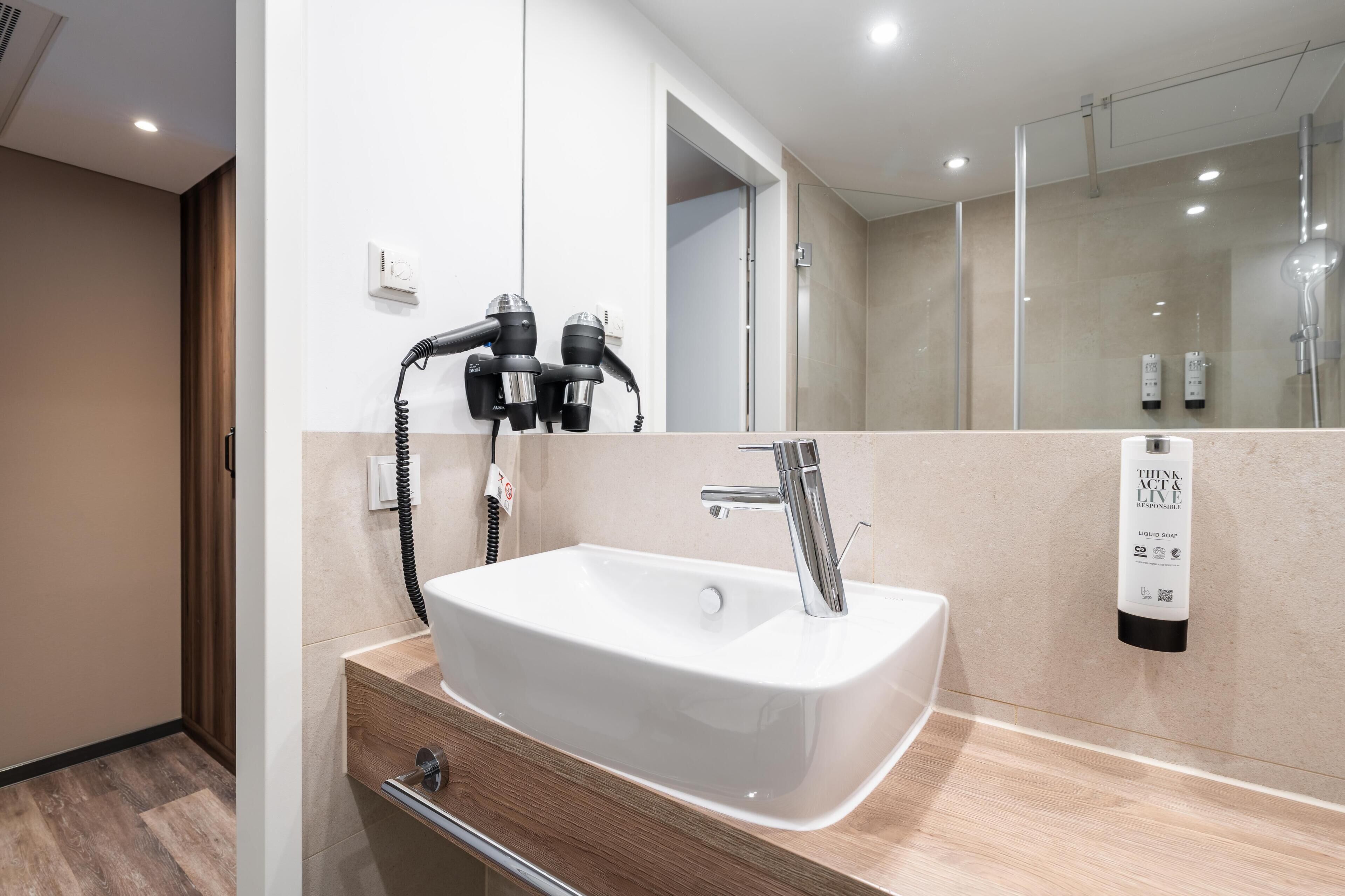 Une salle de bain moderne avec un lavabo blanc, un miroir et un sèche-cheveux fixé au mur.