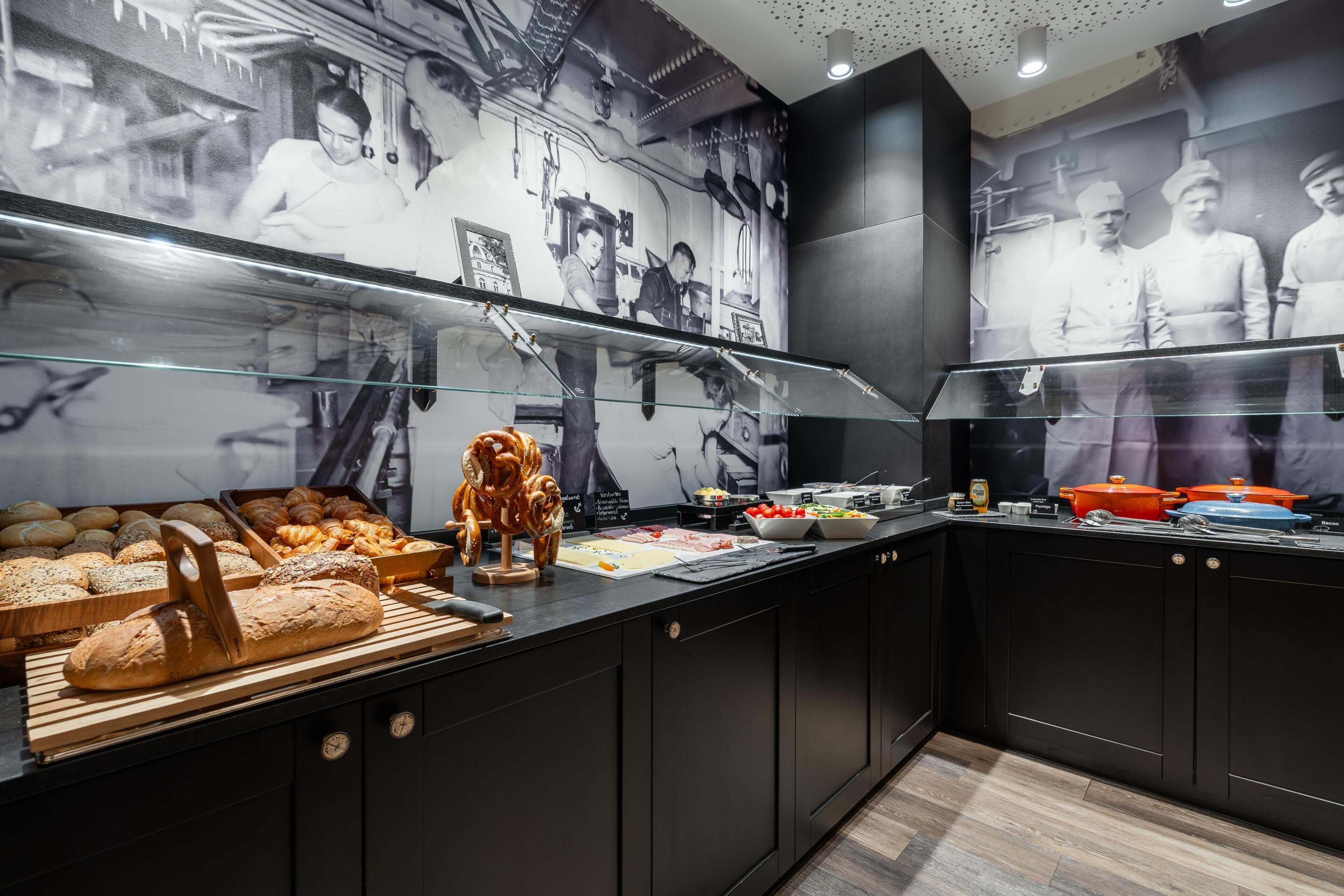 Eine Theke einer Bäckerei mit verschiedenen Backwaren, einem Brot-Schneider und einer Wand mit historischen Fotografien.