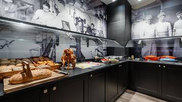 Eine Theke einer Bäckerei mit verschiedenen Backwaren, einem Brot-Schneider und einer Wand mit historischen Fotografien.