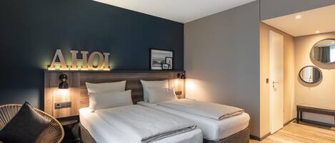Una habitación de hotel moderna con dos camas, una lámpara fijada a la pared, un cuadro enmarcado y un banco.