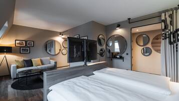A modern hotel room with a large bed, a sofa, a TV, and multiple mirrors.