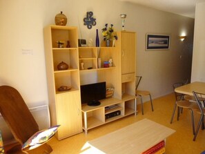 Un ambiente compatto con un mobile TV in legno, un tavolo da pranzo con sedie e una libreria piena di oggetti.