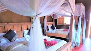 Een kamer met twee bedden, elk met een hemelbedovertrek en kussens. De bedden zijn van hout met een eenvoudig hoofdeinde.