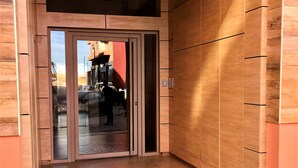 Ein Gebäudeeingang mit Glastür, Holzverkleidung und Fliesenboden.
