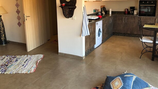 A modern kitchen with a built-in washing machine, a dining area with a table and chairs, and a patterned rug on the floor.