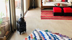 Ein Wohnzimmer mit einer Couch, roten Hocker, einem gemusterten Teppich, einem Tisch mit roter Vase und einer Lampe.