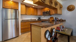 A kitchen with wooden cabinets, a stainless steel refrigerator, a microwave, and a wooden island with a sink. - Honu Kai@Turtle Bay- Pool, AC, Golf, Beach (Kahuku)