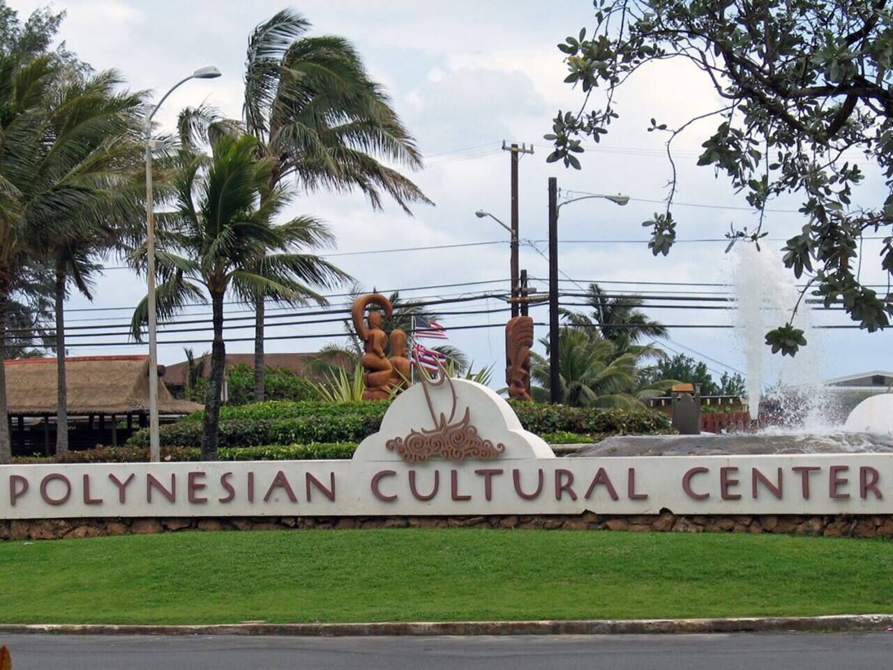 The Polynesian Cultural Center sign with a fountain and palm trees in the background.