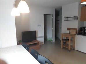 A compact kitchen with a refrigerator, a microwave, and a coffee maker. There's a wooden table with chairs and a television on a stand. - Ski-in/Ski-out: Cozy Apartment for 6 with Mountain Views, Parking & Modern Amenities (Arette)