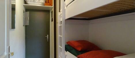 A compact room with a bunk bed, a small closet, and a door leading to another room.