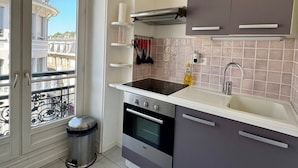 A modern kitchen with a built-in oven, a sink, and a stove. There is a trash bin next to the window, and a view of buildings outside.