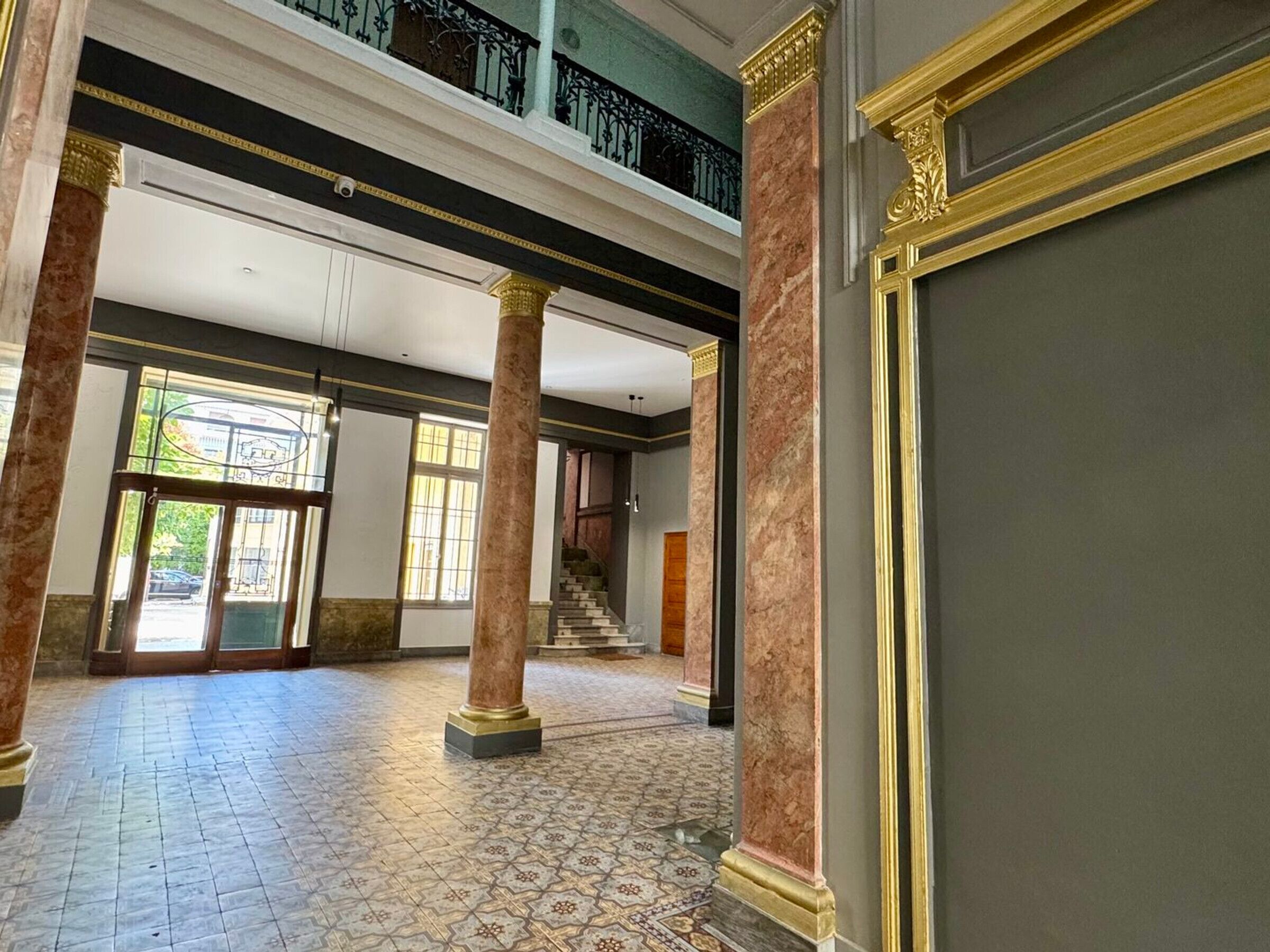 Eine geräumige Lobby mit Marmorsäulen, einem gemusterten Boden und einer Treppe, die in eine obere Ebene führt.