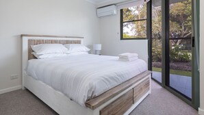 Ein Schlafzimmer mit Bett, Nachttischlampe, Fenster und Blick ins Freie.
