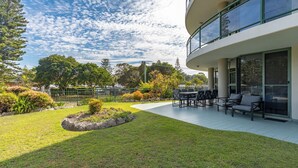 Ein modernes Gebäude mit einer Terrasse, Sitzgelegenheiten im Freien und einem angelegten Garten.