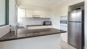 A modern kitchen with white cabinets, a stainless steel refrigerator, a microwave, and a sink.