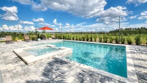 A rectangular swimming pool with a hot tub, surrounded by a paved deck and a fence.