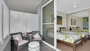 Et moderne soveværelse med en stor seng, to mindre senge, et siddeområde med fletningsmøbler og en skydedør til en balkon.